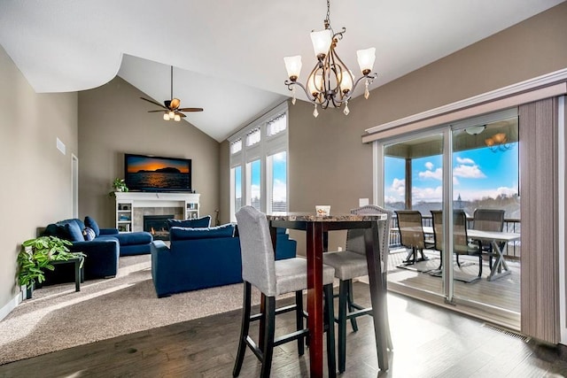 dining area with ceiling fan with notable chandelier, a fireplace, high vaulted ceiling, and wood-type flooring