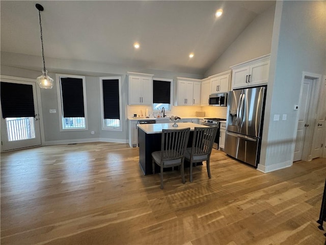 kitchen with white cabinetry, light wood-type flooring, high vaulted ceiling, a kitchen island, and appliances with stainless steel finishes