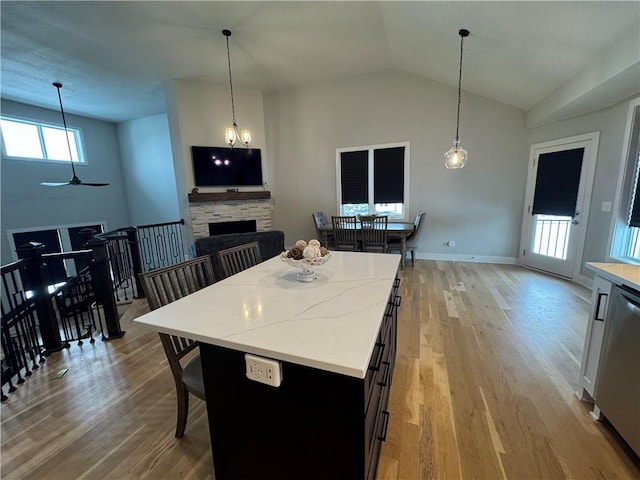 kitchen with dishwasher, a kitchen island, lofted ceiling, ceiling fan with notable chandelier, and a fireplace