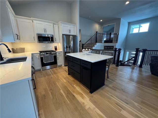 kitchen featuring a center island, light wood-type flooring, white cabinets, appliances with stainless steel finishes, and sink