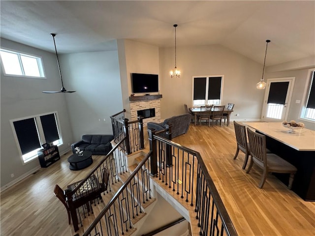 interior space featuring light wood-type flooring, a stone fireplace, vaulted ceiling, and ceiling fan with notable chandelier