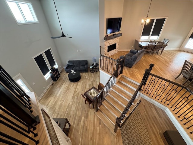 living room featuring a towering ceiling, hardwood / wood-style flooring, a fireplace, and ceiling fan with notable chandelier