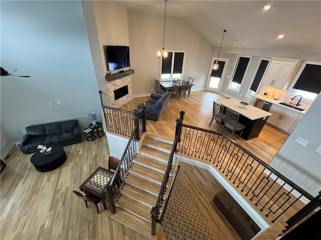 staircase featuring a stone fireplace, hardwood / wood-style floors, lofted ceiling, and a chandelier