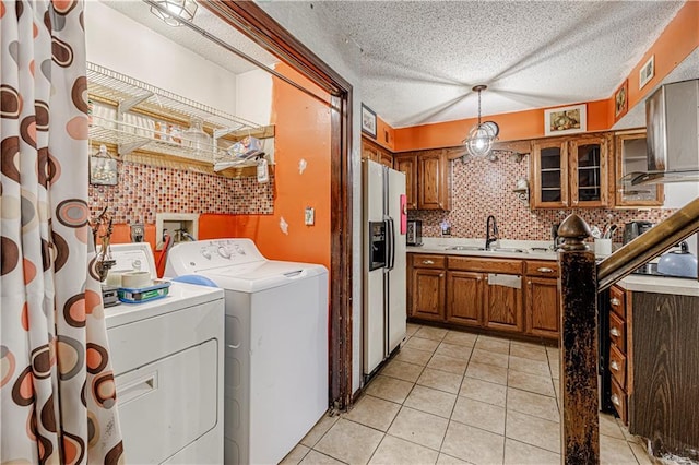 clothes washing area with laundry area, light tile patterned floors, washing machine and clothes dryer, a textured ceiling, and a sink