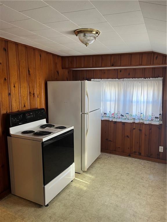 kitchen featuring lofted ceiling, white appliances, and wood walls