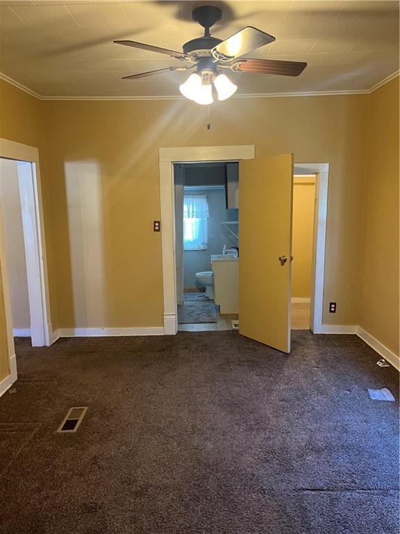 unfurnished bedroom featuring ornamental molding, dark colored carpet, and ceiling fan