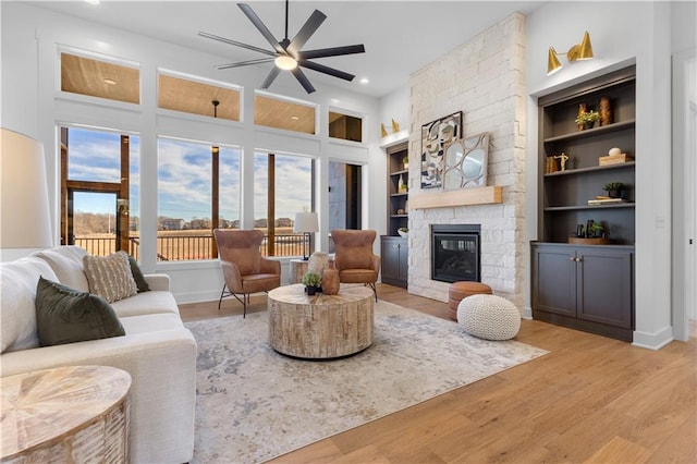 living room featuring ceiling fan, a fireplace, light hardwood / wood-style floors, and built in features