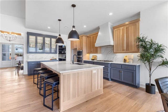 kitchen with decorative light fixtures, gray cabinets, an island with sink, custom range hood, and light stone countertops