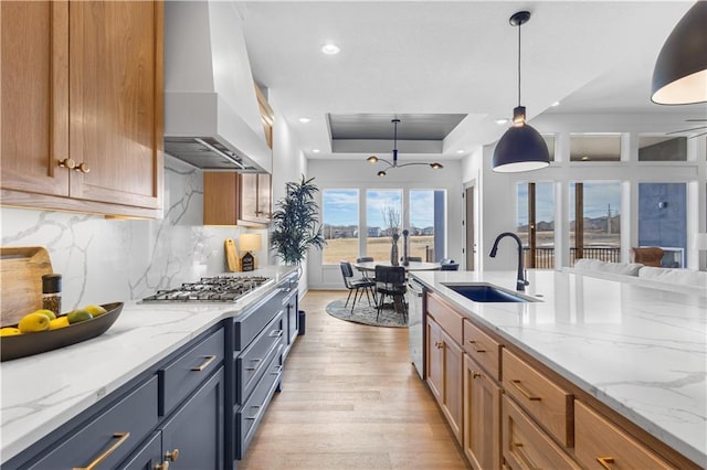 kitchen with decorative light fixtures, sink, light stone counters, a tray ceiling, and wall chimney range hood