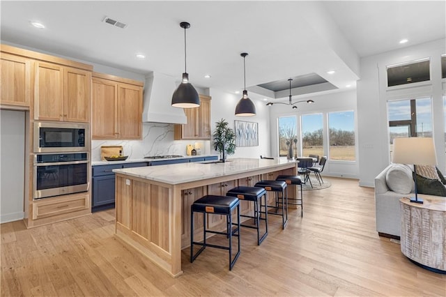 kitchen with pendant lighting, sink, appliances with stainless steel finishes, light stone countertops, and a center island with sink