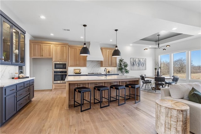 kitchen with custom range hood, oven, black microwave, and a center island with sink