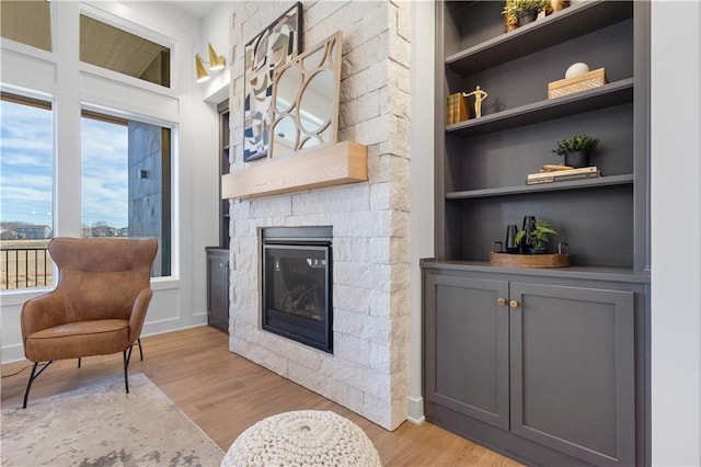 living room featuring built in shelves, a fireplace, and light wood-type flooring