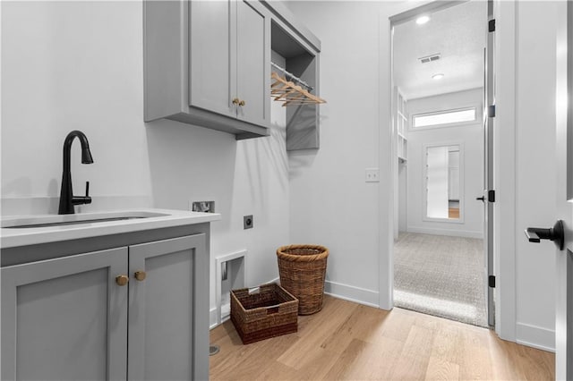 laundry area featuring cabinets, sink, hookup for an electric dryer, and light hardwood / wood-style flooring