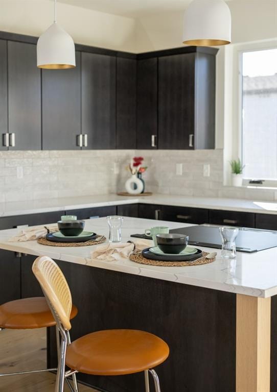 kitchen featuring dark cabinetry, a breakfast bar, hanging light fixtures, backsplash, and a center island