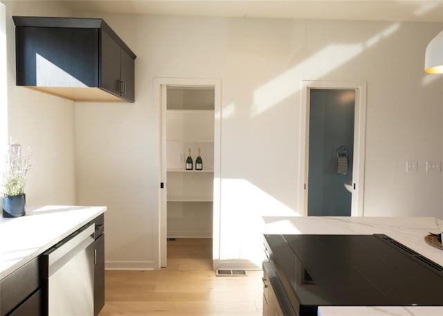 kitchen with light stone counters, visible vents, light wood-style floors, dishwasher, and dark cabinets