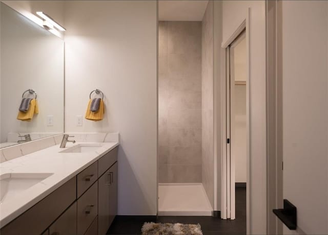 full bath featuring a sink, tiled shower, and double vanity