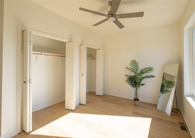 bedroom featuring light wood finished floors, visible vents, two closets, ceiling fan, and baseboards