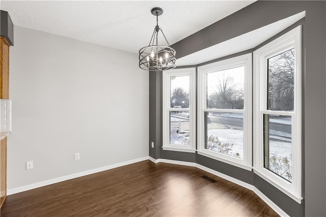 unfurnished dining area featuring dark wood-type flooring, a textured ceiling, and an inviting chandelier