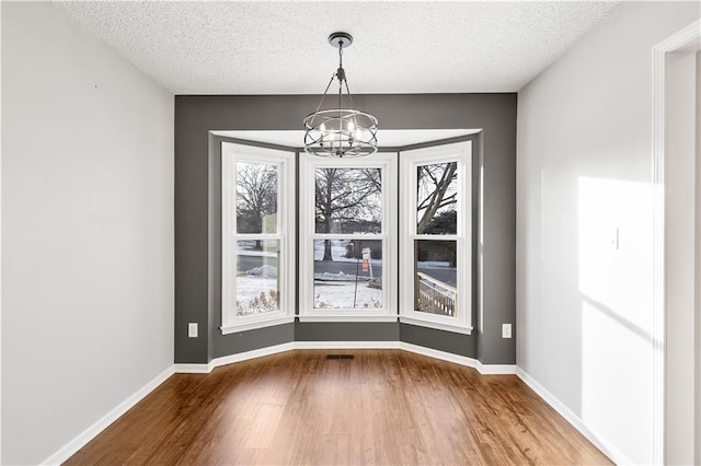 unfurnished dining area featuring hardwood / wood-style floors, a chandelier, and a textured ceiling