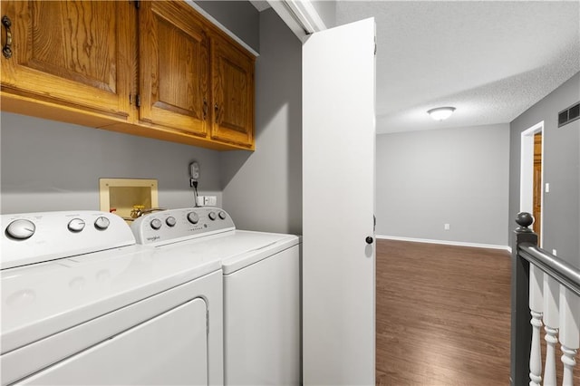 washroom featuring washing machine and clothes dryer, a textured ceiling, dark wood-type flooring, and cabinets