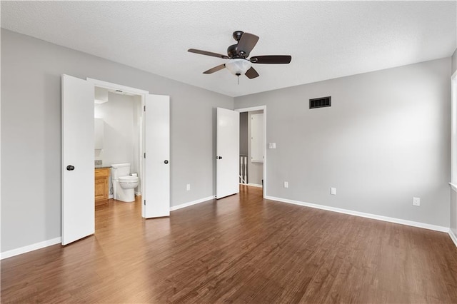 unfurnished bedroom featuring ceiling fan, dark hardwood / wood-style floors, a textured ceiling, and ensuite bath