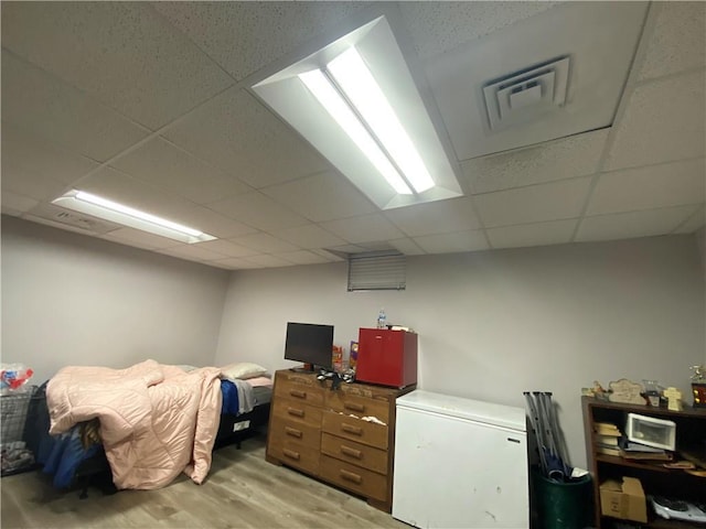 bedroom featuring visible vents, light wood-style flooring, white refrigerator, and a drop ceiling