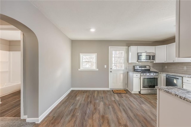 kitchen featuring light stone countertops, appliances with stainless steel finishes, white cabinetry, tasteful backsplash, and light wood-type flooring