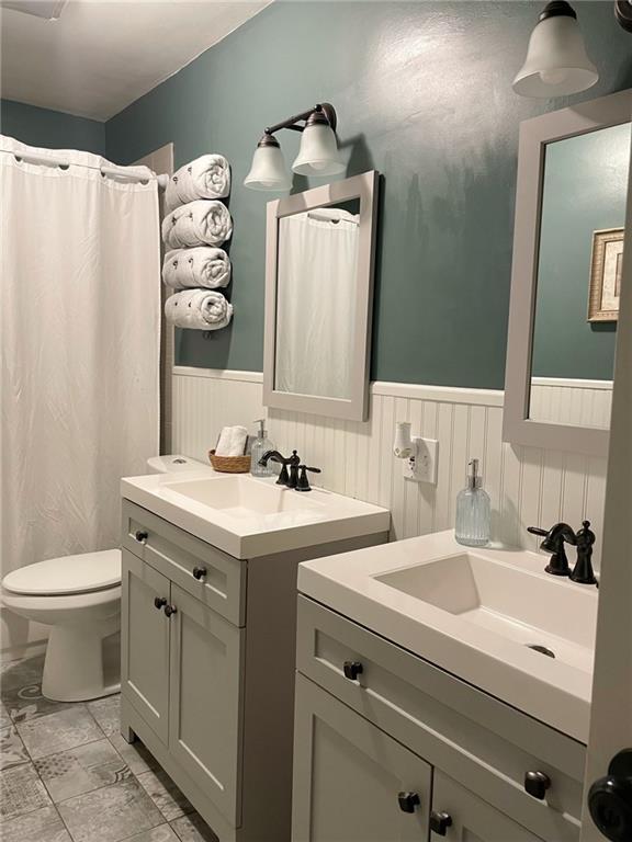 full bath featuring toilet, a wainscoted wall, two vanities, and a sink