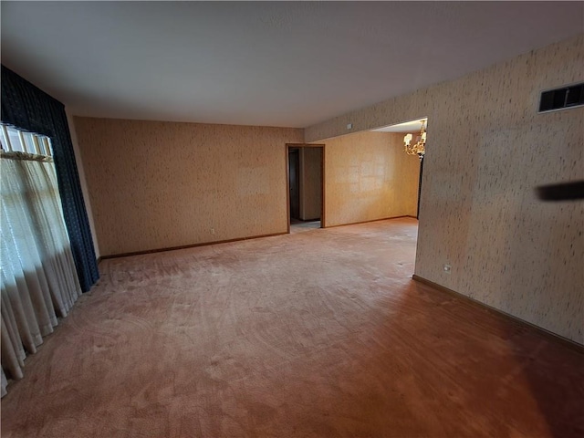 carpeted empty room featuring an inviting chandelier