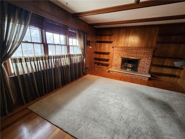 living room featuring beamed ceiling, wooden walls, a fireplace, and light hardwood / wood-style flooring