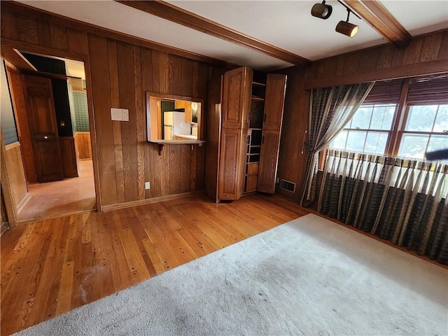 interior space featuring wooden walls, beamed ceiling, and light wood-type flooring