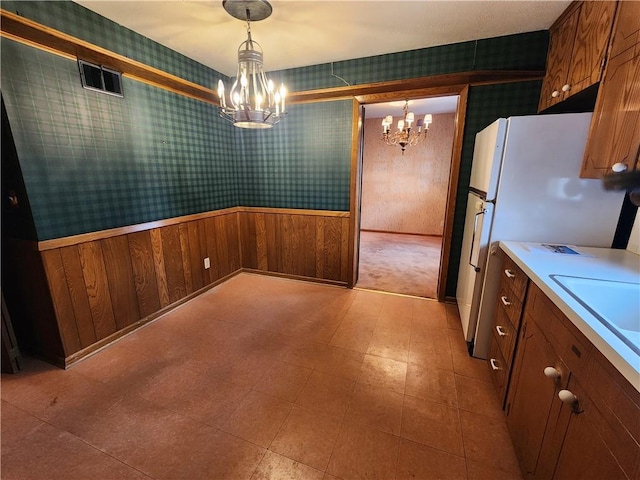 kitchen with hanging light fixtures, wooden walls, a chandelier, and white refrigerator