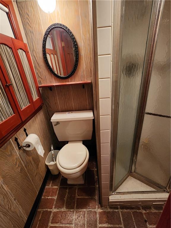 bathroom featuring a shower with shower door, wooden walls, and toilet