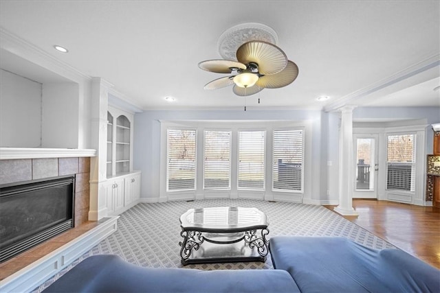 living room with ceiling fan, a tile fireplace, crown molding, and decorative columns