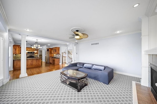 living room featuring ceiling fan with notable chandelier, carpet, crown molding, and a fireplace