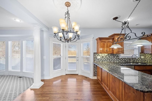 kitchen featuring hanging light fixtures, ornate columns, and dark stone counters