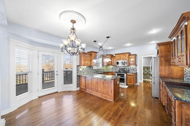 kitchen with appliances with stainless steel finishes, dark hardwood / wood-style flooring, tasteful backsplash, hanging light fixtures, and a notable chandelier