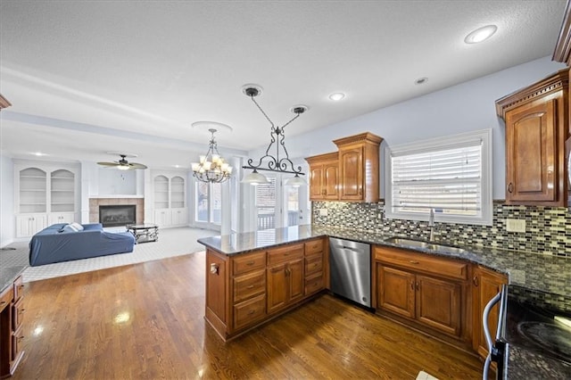 kitchen with pendant lighting, sink, kitchen peninsula, stainless steel dishwasher, and a tiled fireplace