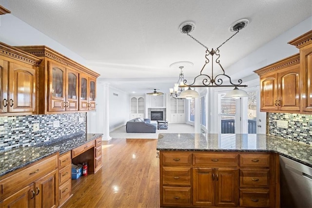 kitchen with decorative light fixtures, tasteful backsplash, dark stone countertops, stainless steel dishwasher, and light hardwood / wood-style flooring