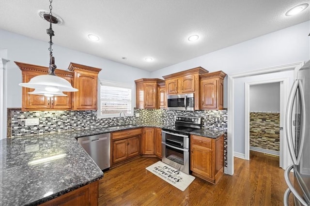 kitchen with appliances with stainless steel finishes, backsplash, dark wood-type flooring, hanging light fixtures, and sink