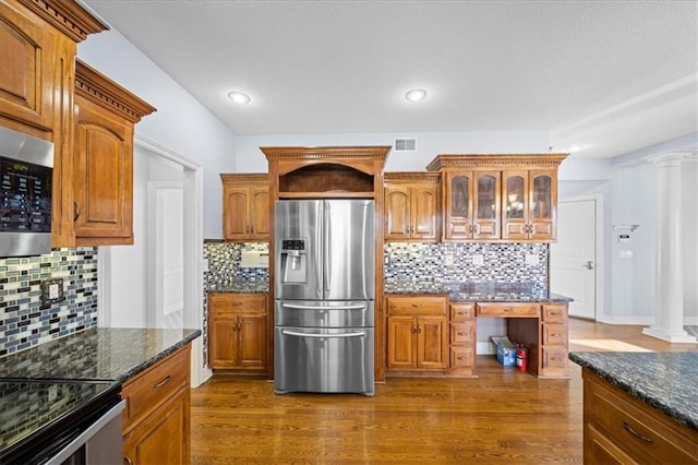 kitchen with decorative columns, stainless steel appliances, tasteful backsplash, dark wood-type flooring, and dark stone countertops