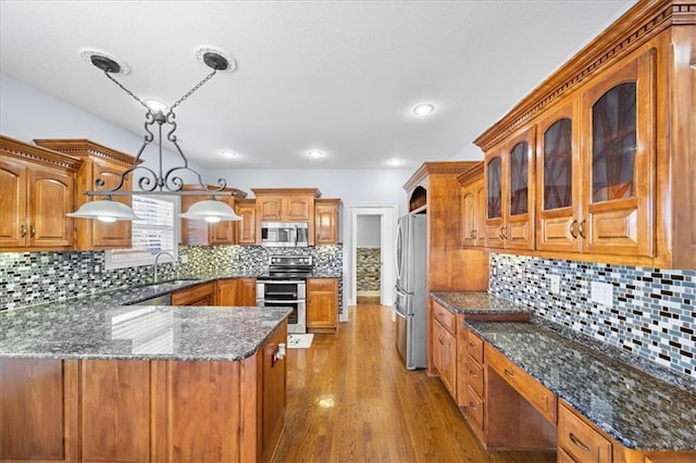 kitchen with pendant lighting, appliances with stainless steel finishes, dark stone countertops, sink, and light hardwood / wood-style flooring