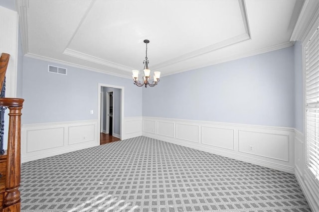 carpeted spare room with a raised ceiling, crown molding, and a chandelier