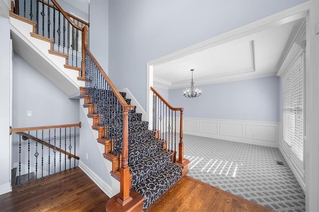 stairs featuring hardwood / wood-style flooring, ornamental molding, and a notable chandelier