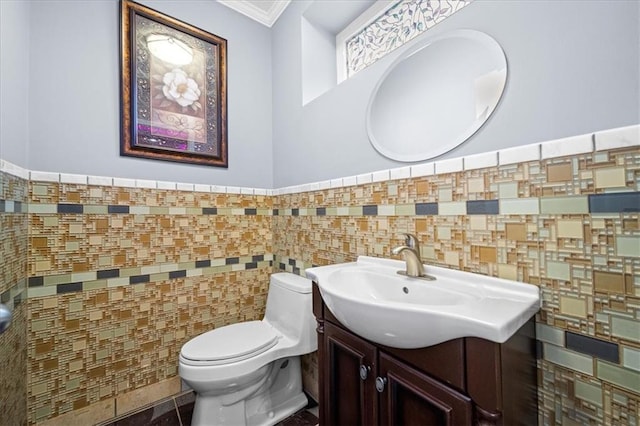 bathroom with toilet, crown molding, vanity, and tile walls