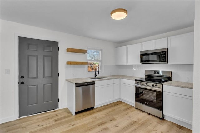 kitchen with light wood-type flooring, appliances with stainless steel finishes, sink, and white cabinetry