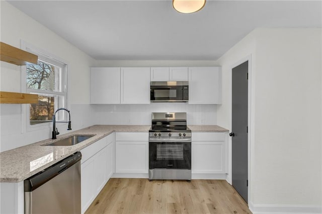 kitchen featuring sink, light wood-type flooring, light stone countertops, stainless steel appliances, and white cabinets