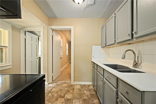 kitchen with sink, a textured ceiling, gray cabinets, and tasteful backsplash