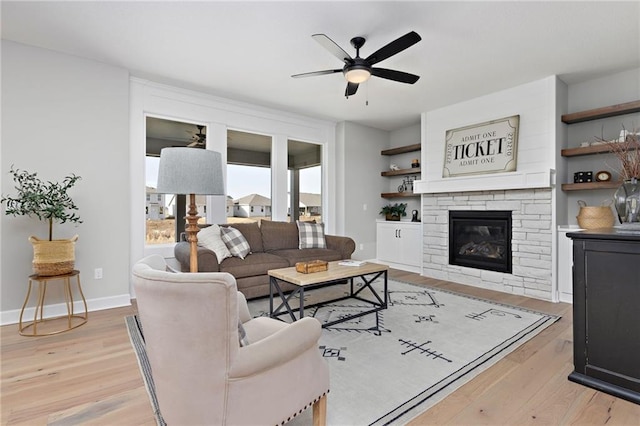 living room featuring ceiling fan, a fireplace, and light wood-type flooring