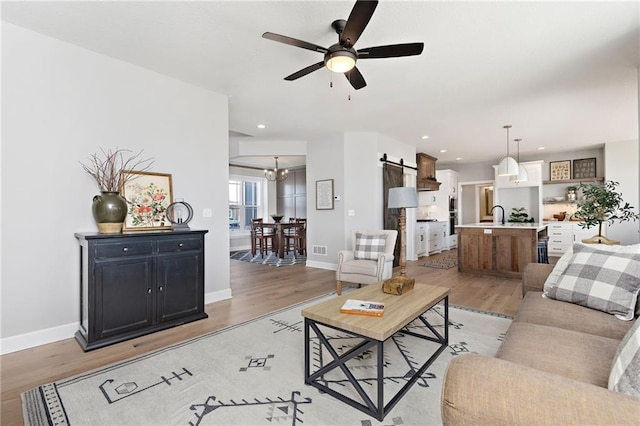 living room with sink, ceiling fan with notable chandelier, light hardwood / wood-style flooring, and a barn door